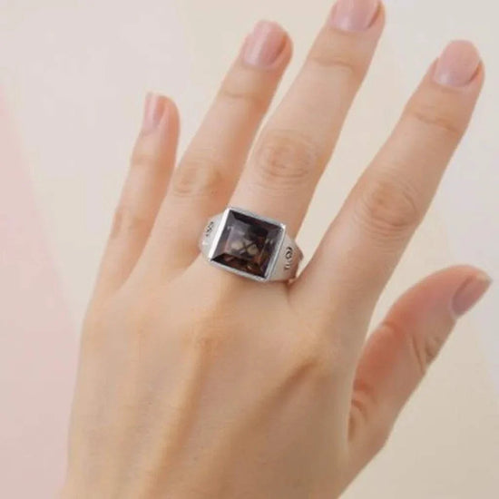 Marcel Drucker designer ring on hand with 5.99 CTW princess-cut brown topaz and diamond accents in sterling silver with white gold rhodium finish